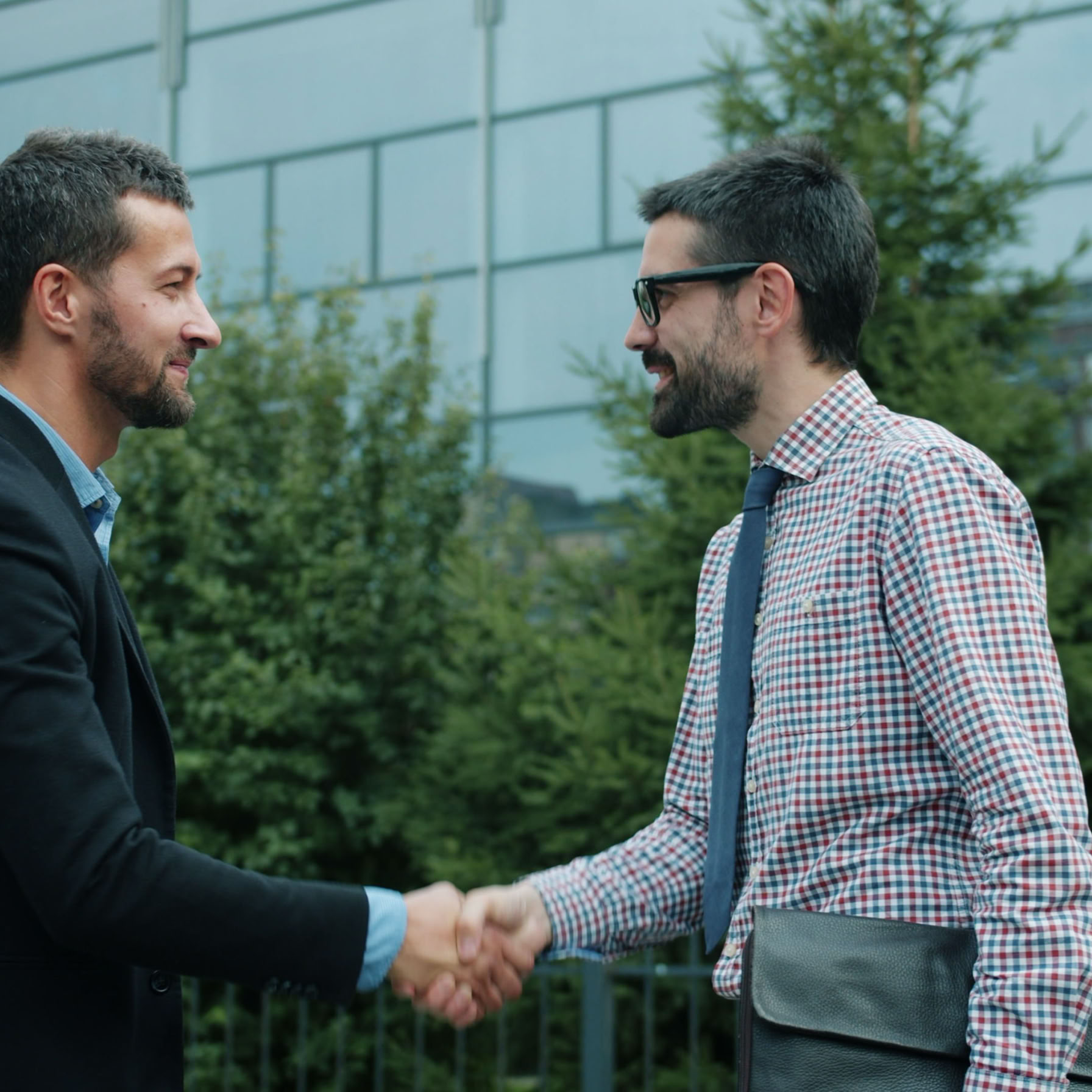 Two men shaking hands outside a modern office building, symbolizing business partnership.