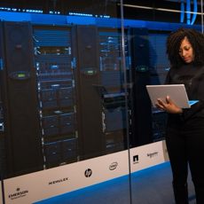 A female engineer using a laptop while monitoring data servers in a modern server room.