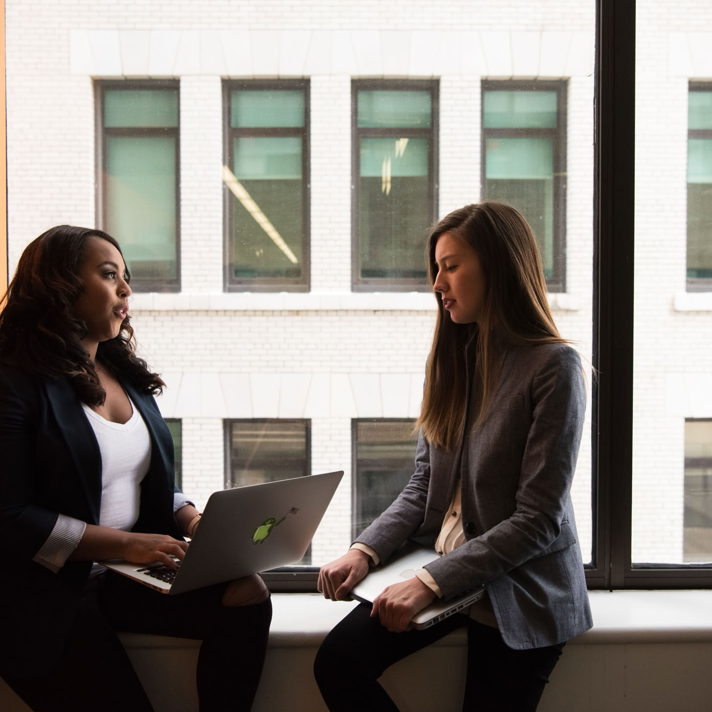 Two women having a business discussion in an office setting, using a laptop.