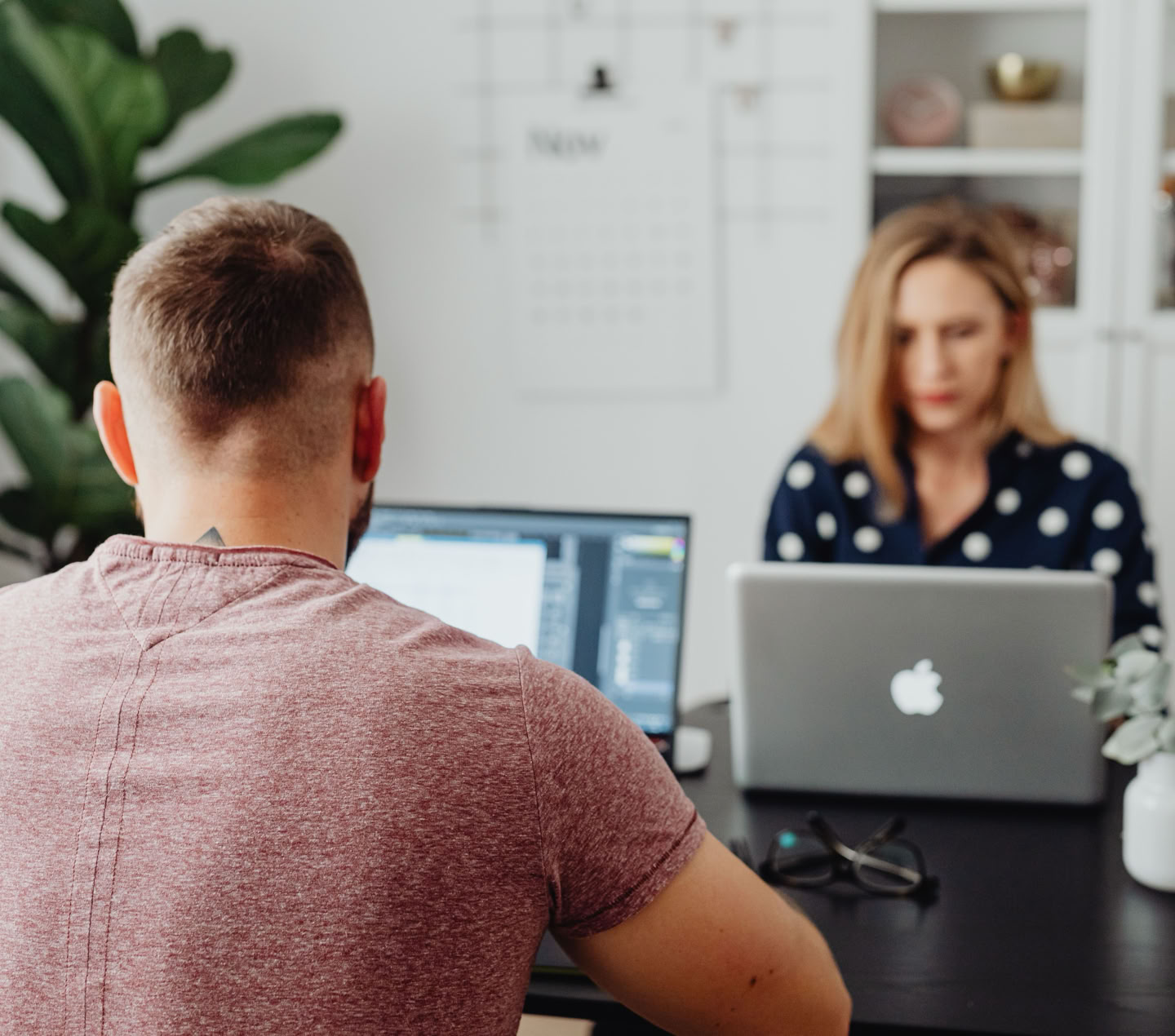 Two professionals working on laptops in a modern office setting.