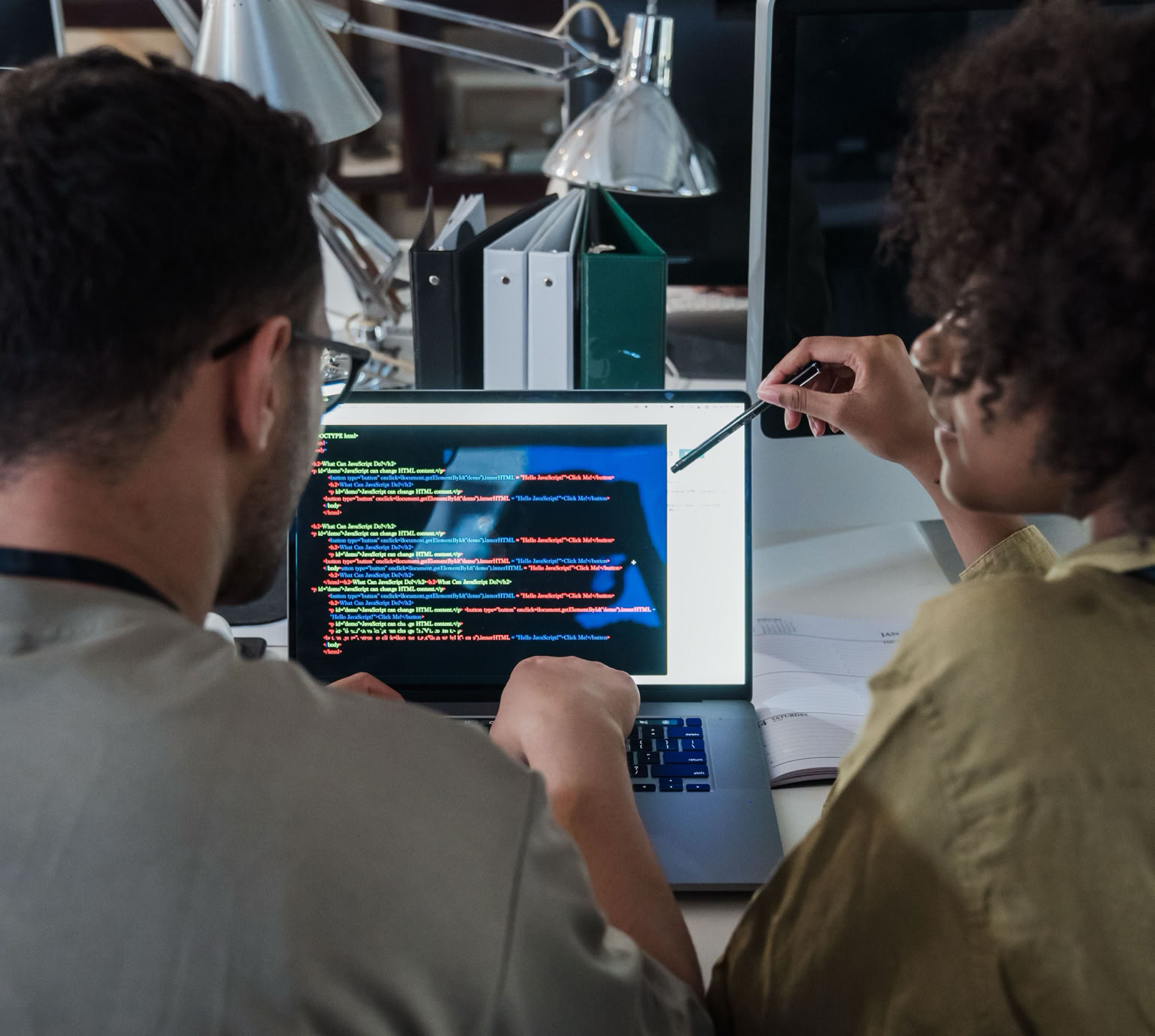Two developers engage in software programming on a laptop in a modern office setting.