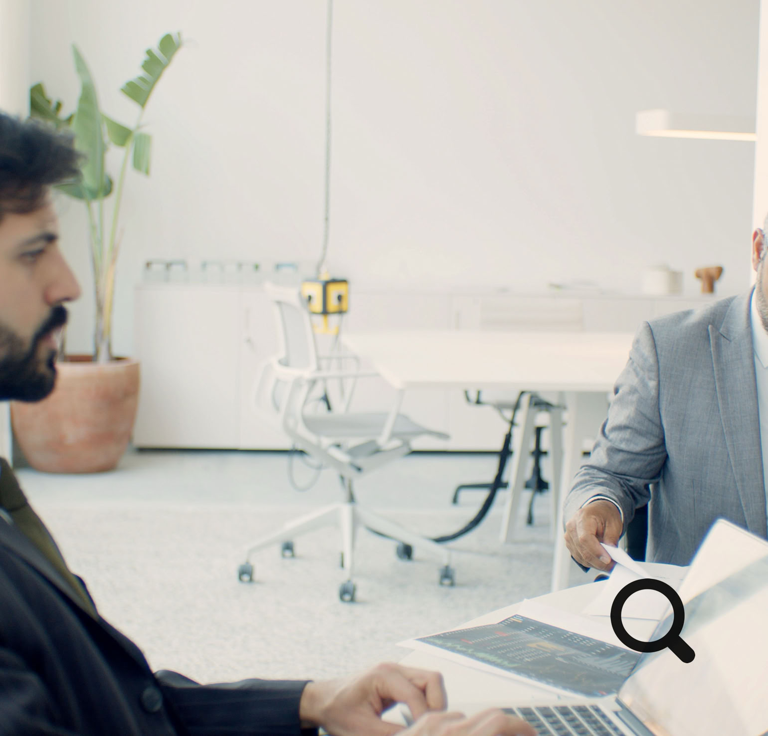 Two businessmen in formal suits working on laptops in a modern office setting.