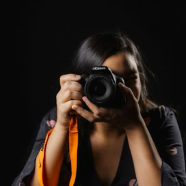 Studio shot of a woman photographer taking a picture with a camera against a black backdrop.