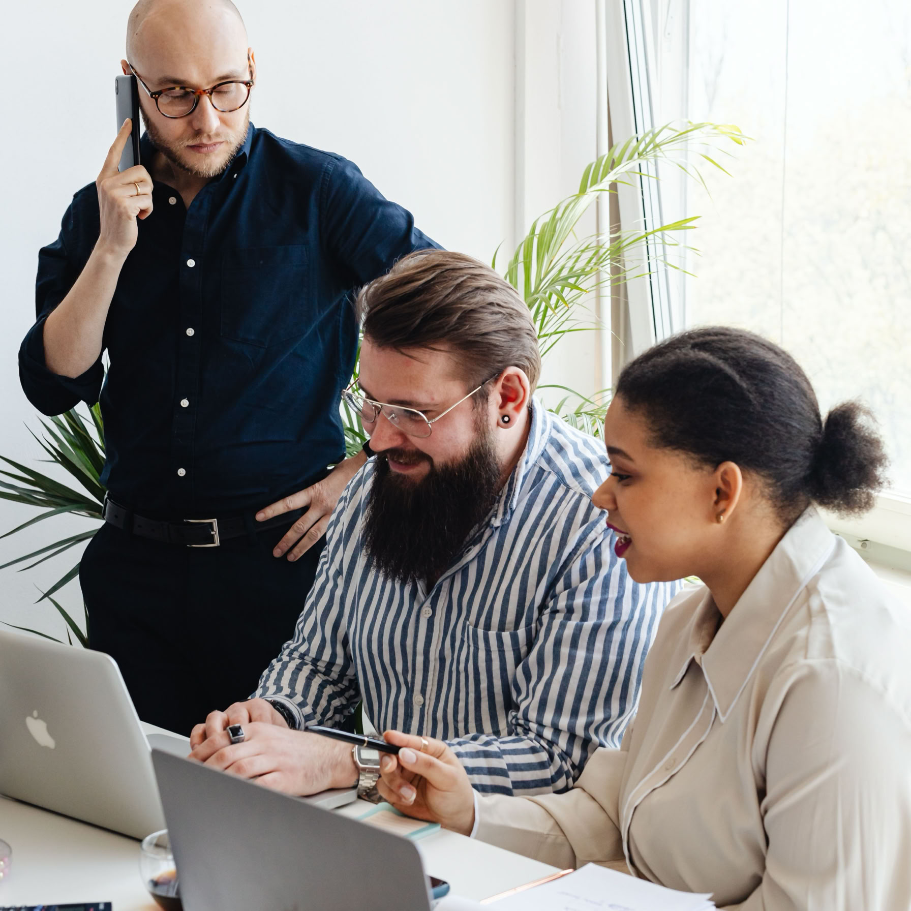 A diverse group of professionals engaged in a collaborative team meeting at a modern office with laptops and mobile phones.